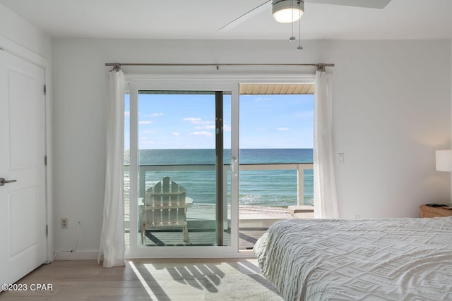 bedroom with wood-type flooring, access to exterior, a water view, a view of the beach, and ceiling fan