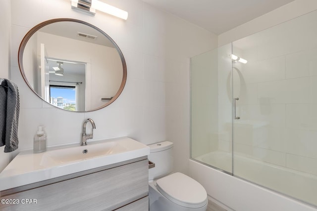 full bathroom featuring tile walls, toilet, vanity, and shower / bath combination with glass door