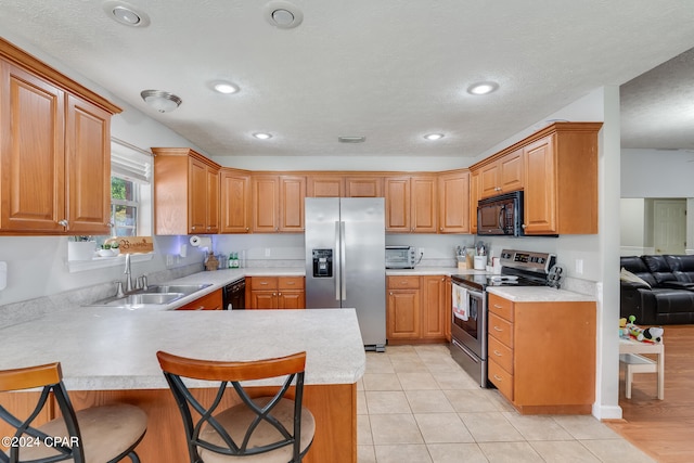 kitchen featuring sink, kitchen peninsula, a kitchen bar, black appliances, and light tile patterned floors