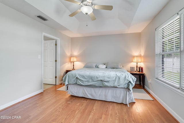 bedroom with light wood-type flooring, a tray ceiling, and ceiling fan