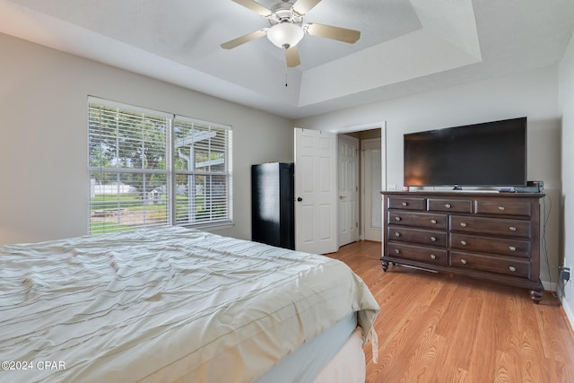 bedroom with light hardwood / wood-style floors, ceiling fan, and a raised ceiling