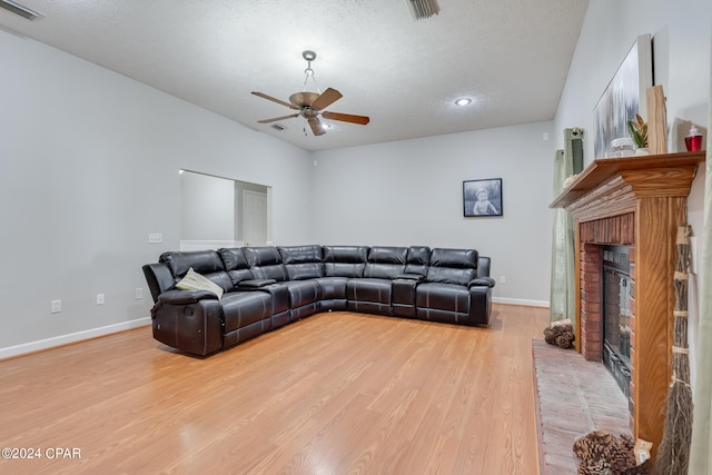 living room featuring a textured ceiling, a fireplace, ceiling fan, and light hardwood / wood-style flooring