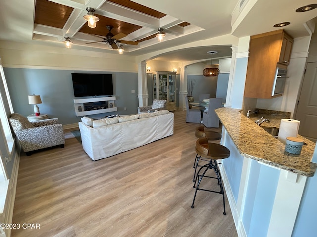 living room featuring ceiling fan, light hardwood / wood-style floors, and coffered ceiling