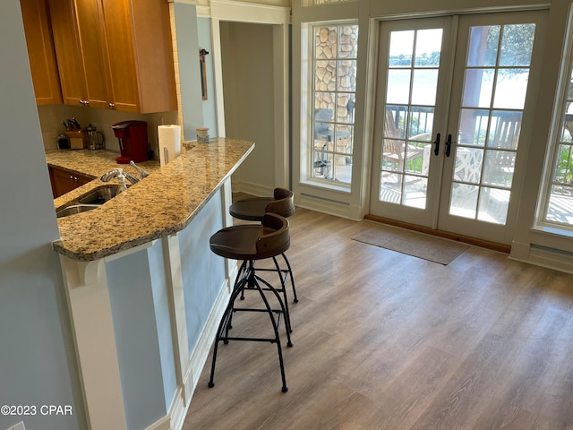 kitchen featuring light hardwood / wood-style floors, light stone counters, kitchen peninsula, a breakfast bar area, and sink