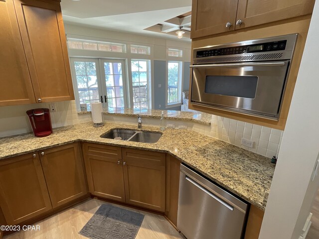 kitchen with light stone counters, light hardwood / wood-style floors, sink, kitchen peninsula, and stainless steel appliances