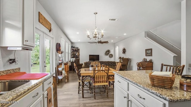 kitchen featuring light stone counters, light wood-type flooring, hanging light fixtures, white cabinetry, and ceiling fan with notable chandelier