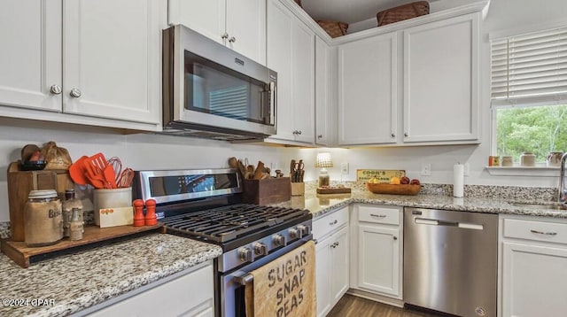 kitchen with light stone counters, white cabinets, stainless steel appliances, and sink