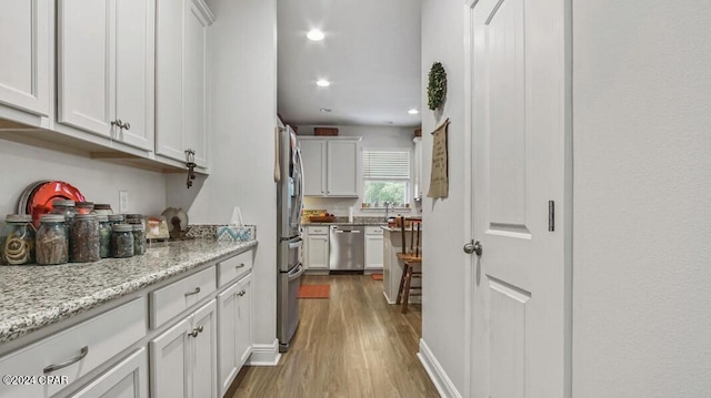 kitchen with light stone counters, white cabinets, appliances with stainless steel finishes, and light hardwood / wood-style floors