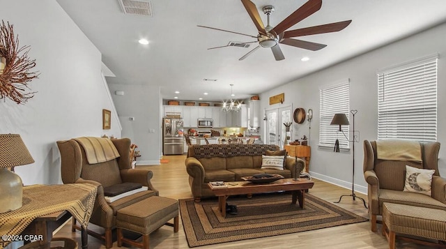 living room featuring ceiling fan with notable chandelier and light wood-type flooring