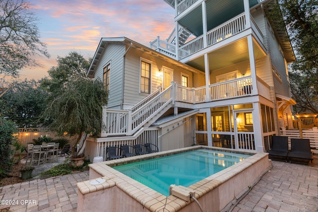 back house at dusk with a balcony and a patio