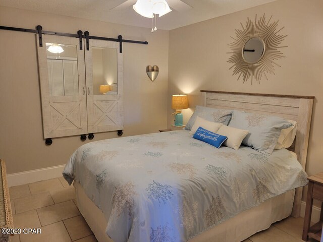 bedroom with a barn door, light tile patterned floors, and ceiling fan