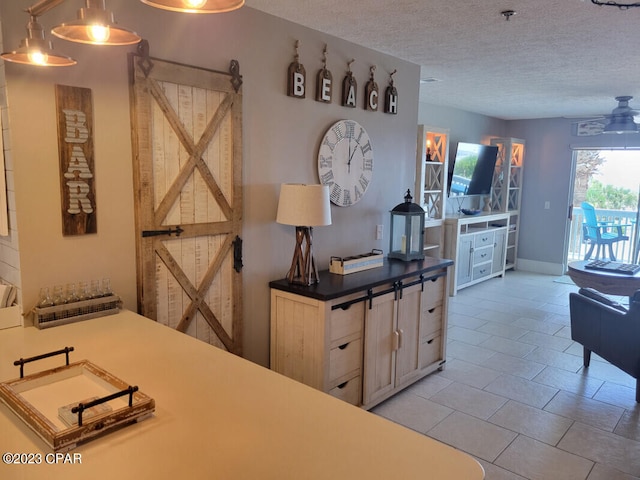 kitchen with light brown cabinets, ceiling fan, a textured ceiling, a barn door, and pendant lighting