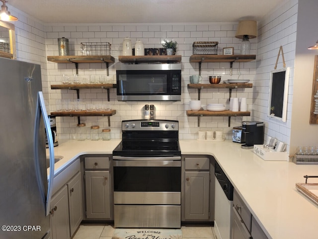 kitchen with light tile patterned flooring, gray cabinetry, backsplash, and appliances with stainless steel finishes