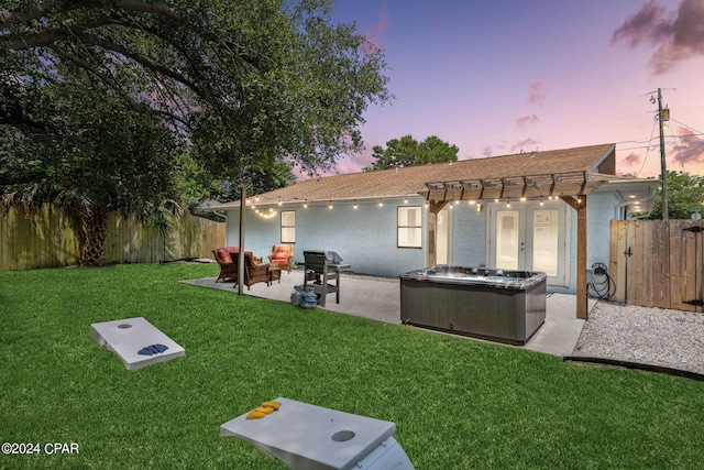 back house at dusk featuring french doors, a patio area, a hot tub, a lawn, and an outdoor hangout area