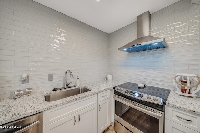 kitchen featuring white cabinetry, wall chimney range hood, sink, and appliances with stainless steel finishes