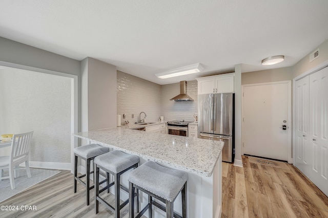 kitchen featuring kitchen peninsula, appliances with stainless steel finishes, sink, wall chimney range hood, and white cabinets