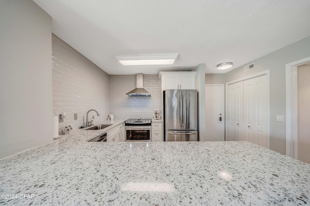 kitchen featuring white cabinetry, appliances with stainless steel finishes, wall chimney range hood, and light stone counters