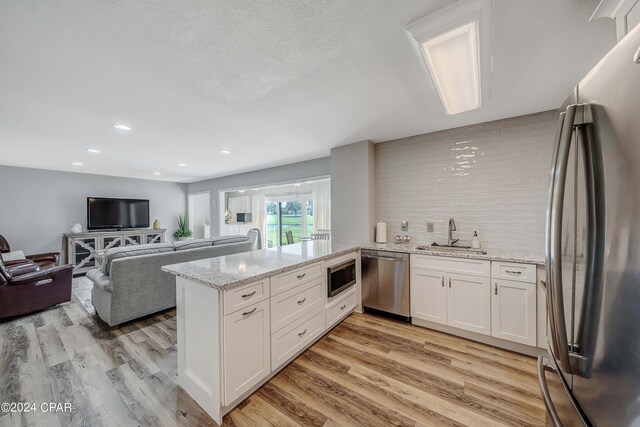 kitchen with kitchen peninsula, appliances with stainless steel finishes, light stone countertops, sink, and white cabinetry