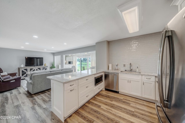 kitchen featuring sink, light wood-type flooring, kitchen peninsula, stainless steel appliances, and white cabinets