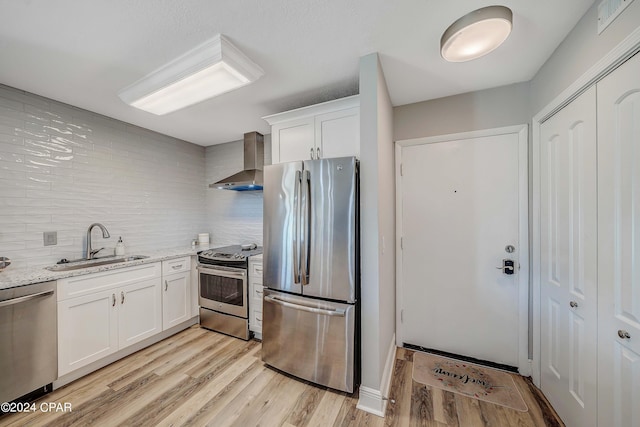 kitchen featuring sink, white cabinetry, stainless steel appliances, light stone countertops, and wall chimney exhaust hood