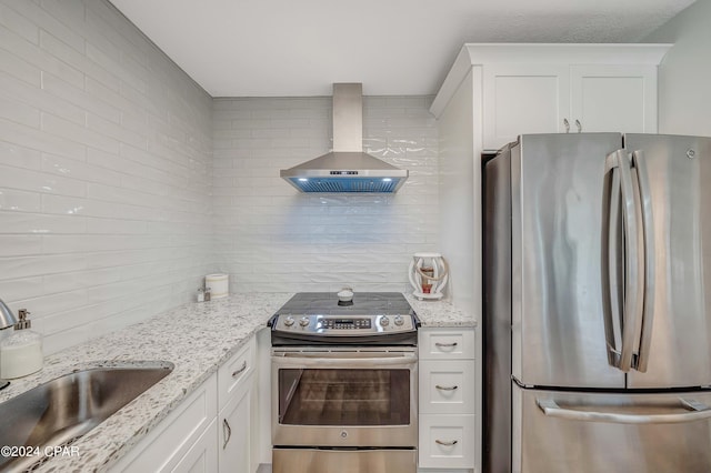 kitchen with light stone countertops, stainless steel appliances, wall chimney range hood, backsplash, and white cabinets