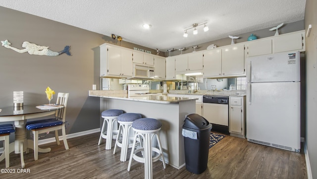 kitchen with a textured ceiling, kitchen peninsula, white cabinetry, and white appliances