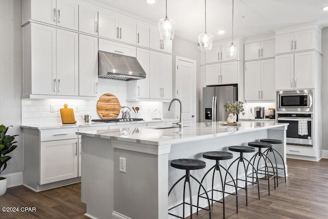 kitchen with exhaust hood, appliances with stainless steel finishes, a kitchen island with sink, and white cabinetry