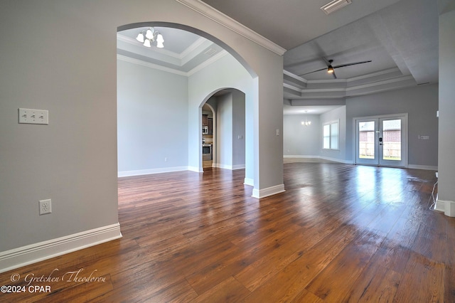 spare room with ceiling fan with notable chandelier, ornamental molding, a raised ceiling, and dark wood-type flooring