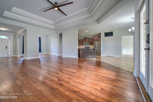 unfurnished living room featuring light wood-type flooring, a raised ceiling, and plenty of natural light