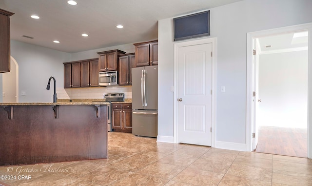 kitchen with kitchen peninsula, backsplash, appliances with stainless steel finishes, a breakfast bar area, and light stone countertops