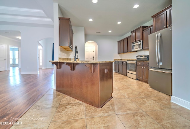 kitchen featuring light stone counters, tasteful backsplash, stainless steel appliances, a breakfast bar area, and light wood-type flooring