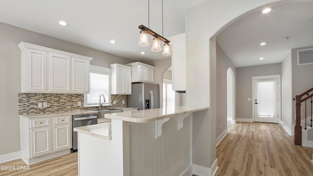 kitchen with pendant lighting, light hardwood / wood-style floors, white cabinetry, kitchen peninsula, and appliances with stainless steel finishes