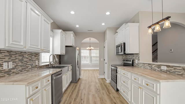 kitchen featuring pendant lighting, stainless steel appliances, white cabinetry, and light wood-type flooring