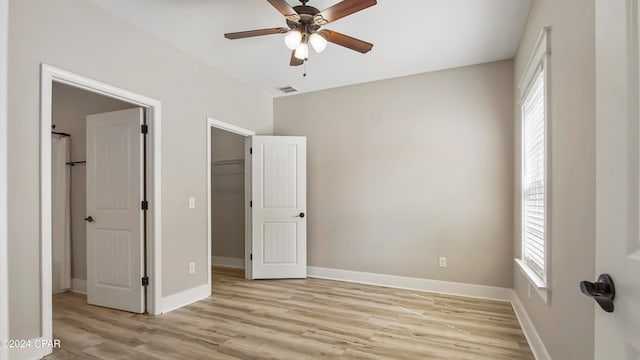 unfurnished bedroom featuring light hardwood / wood-style flooring, multiple windows, a walk in closet, and ceiling fan