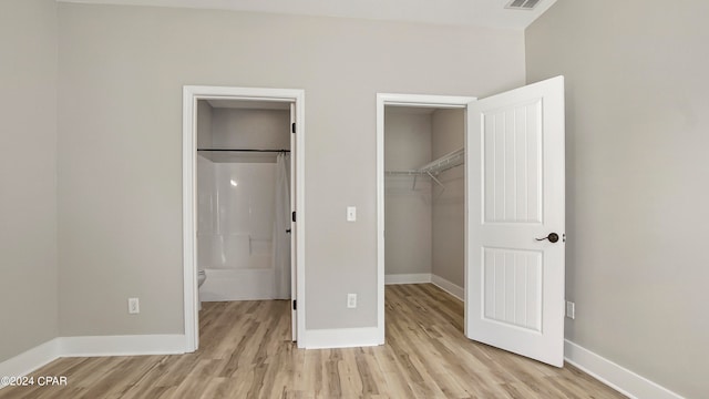 unfurnished bedroom featuring light hardwood / wood-style flooring, ensuite bathroom, and a walk in closet