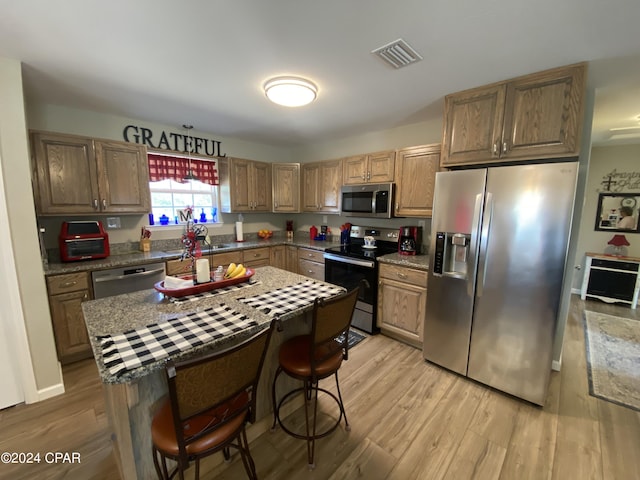 kitchen with a kitchen breakfast bar, sink, light wood-type flooring, appliances with stainless steel finishes, and a kitchen island