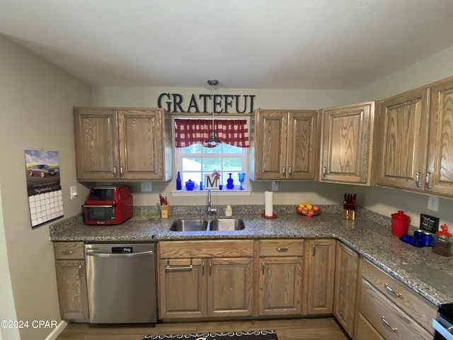 kitchen with decorative light fixtures, stainless steel dishwasher, dark stone counters, and sink