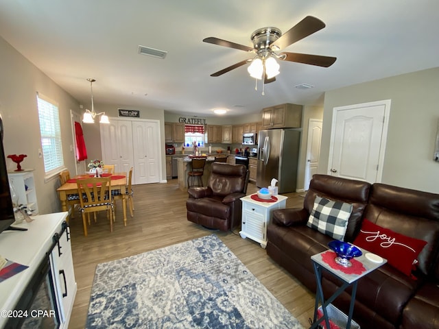 living room with a wealth of natural light, light hardwood / wood-style floors, and ceiling fan with notable chandelier