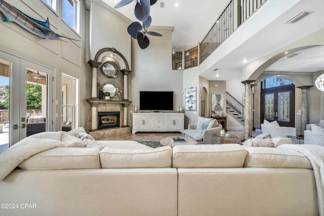 living room with a high ceiling, a premium fireplace, french doors, ceiling fan, and decorative columns