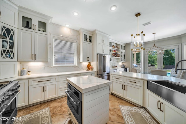 kitchen with decorative light fixtures, backsplash, high end appliances, and white cabinetry