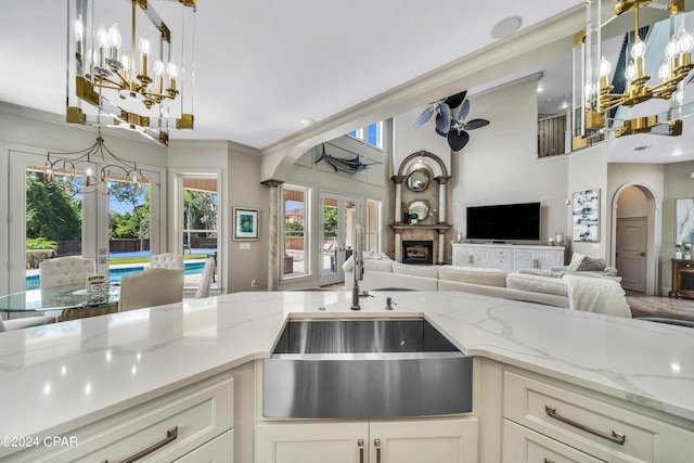 kitchen with ceiling fan with notable chandelier, decorative light fixtures, french doors, sink, and light stone counters