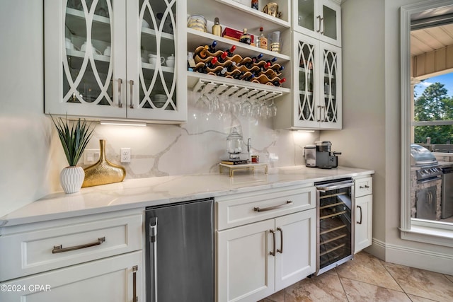 bar with light stone countertops, backsplash, refrigerator, and beverage cooler