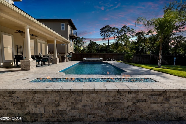 pool at dusk featuring pool water feature, an in ground hot tub, a patio, and ceiling fan