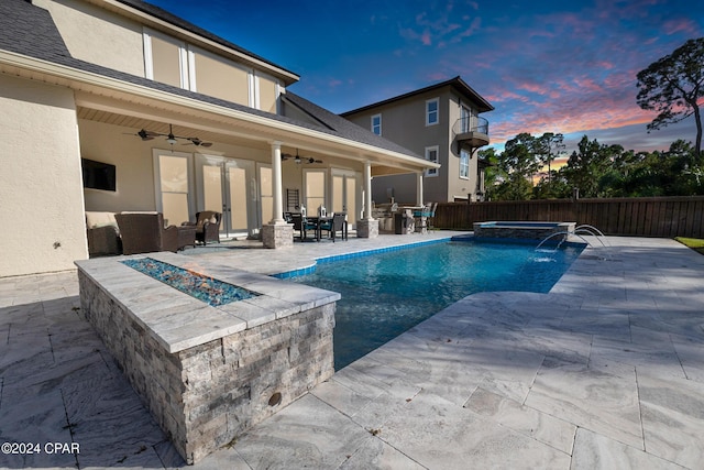 pool at dusk with ceiling fan, an in ground hot tub, an outdoor living space with a fire pit, pool water feature, and a patio area