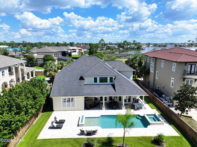 back of house featuring a swimming pool with hot tub, an outdoor living space with a fire pit, a lawn, and a patio