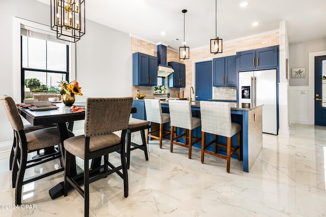 kitchen featuring a kitchen breakfast bar, blue cabinets, high quality fridge, decorative light fixtures, and wall chimney range hood