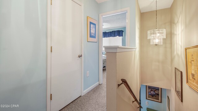 hallway with a textured ceiling, a notable chandelier, and light carpet