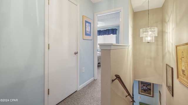 hallway featuring carpet flooring, a textured ceiling, baseboards, a notable chandelier, and an upstairs landing