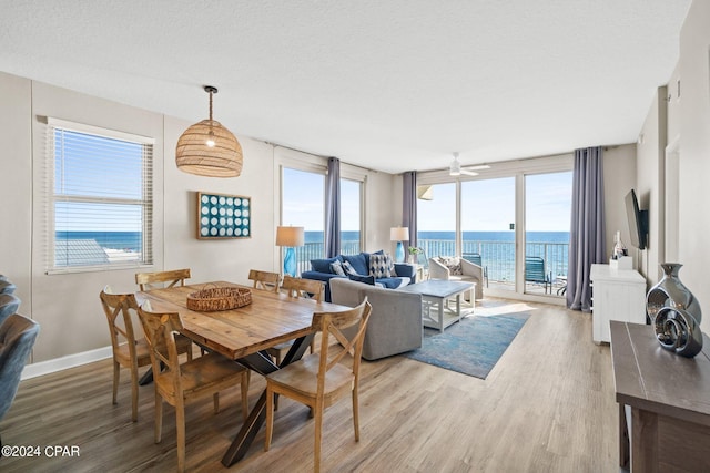 dining space with ceiling fan, light hardwood / wood-style flooring, a water view, and a healthy amount of sunlight