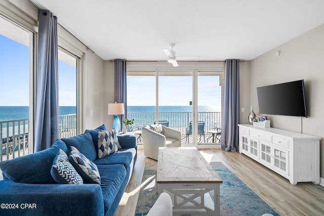 living room featuring light wood-type flooring, a water view, ceiling fan, and plenty of natural light